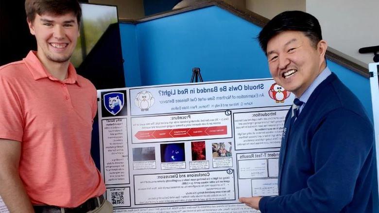 Two people stand in front of a research poster. 